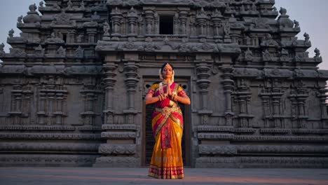 indian classical dancer is gracefully posing in front of a temple at dawn, her colorful costume contrasting with the ancient stone architecture, creating a serene and spiritual atmosphere