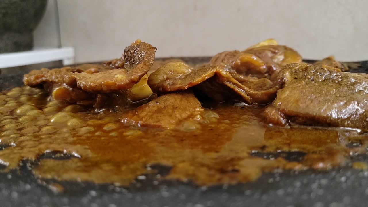 Marinated lamb sizzles on a flat griddle, releasing a delicious, mouth-watering aroma. The cooking process creates an enticing scene for food lovers.