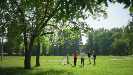 two elderly men are seen standing in front of a goalpost, instructing a younger boy to position himself by the post, the man is holding a ball in his hand