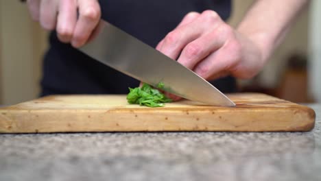 adult uses sharp knife to slice basil on wooden cutting board