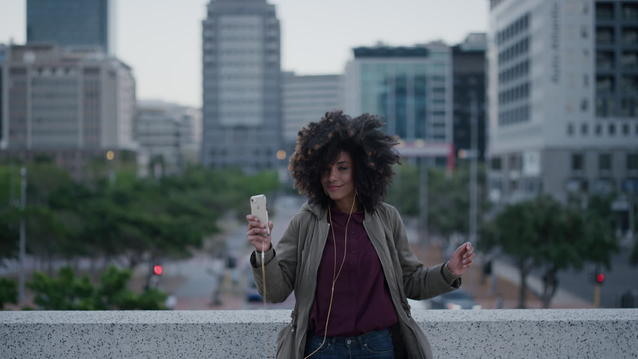 portrait young happy african american woman student wearing earphones listening to music dancing jumping enjoying successful urban lifestyle lively black female student celebrating slow motion afro hairstyle