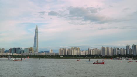 Horizonte-De-La-Ciudad-De-Seúl:-Gente-Haciendo-Kayak,-Montando-Windsurf,-Remando-En-El-Río-Han,-El-Centro-De-Seúl-En-La-Colorida-Puesta-De-Sol-Rosada,-La-Torre-Lotte-World-En-El-Fondo