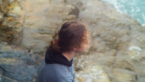 Thoughtful-Young-Teenager-Lad-Sitting-on-a-Rock-Watching-Ocean-Breaking-Waves