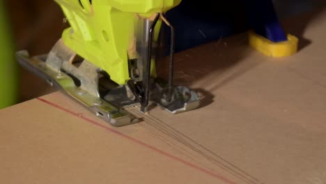 close-up of electric jigsaw in action, men's hand cutting up wood board with a jigsaw