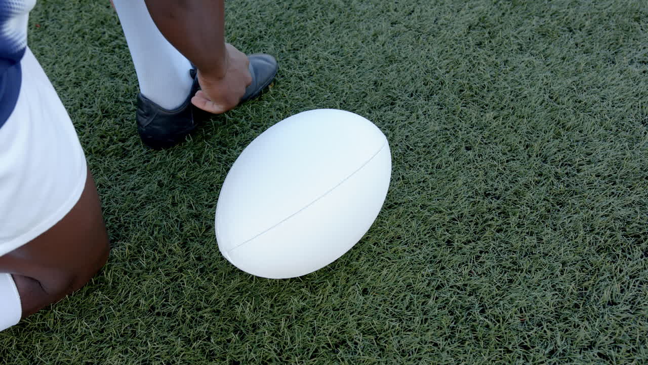 Amarrando os cadarços, jogador de rugby masculino afro-americano preparando-se para o jogo em campo gramado, espaço para texto