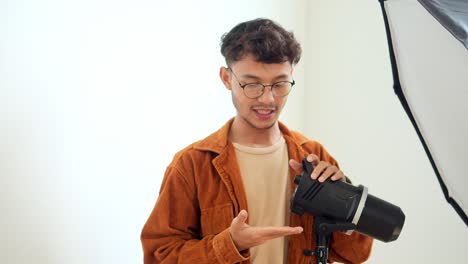 Young Asian Man Photographer Setting Up And Adjusting His Professional Studio Lighting Equipment