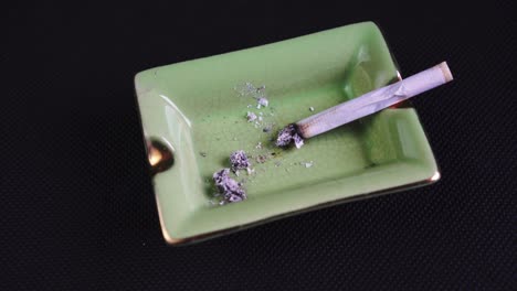 Smoking-and-Ashing-a-Rolled-Cigarette-or-Joint,-legalised-marijuana-on-green-Ashtray