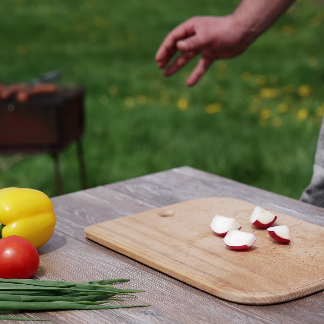 Hombre cortando rábanos para una barbacoa. Verduras frescas en la mesa con el fondo de un brasero con carne a la parrilla. Momento para un picnic.