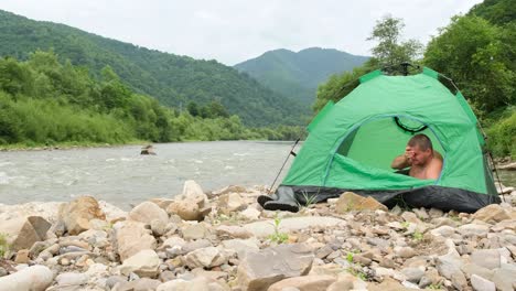 a lonely man wakes up in the morning in a tent he spent the night by a mountain river a lonely man wakes up in the morning in a tent he spent the night by a mountain river holidays in the mountains alone