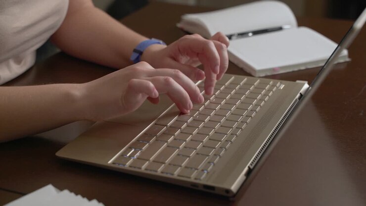 Female hands are typing text on laptop keyboard. Fingers quickly press the keys on the keyboard. There is notebook next to it. Personal computer, remote work at home, business, study, messaging, chat