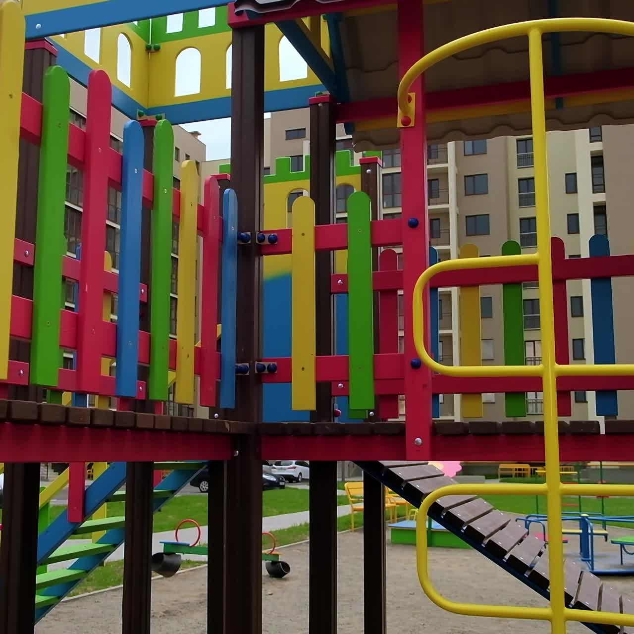 Approaching a nice bright playground for kids with slides and ladders. Residential area with playground in the middle. Low angle view