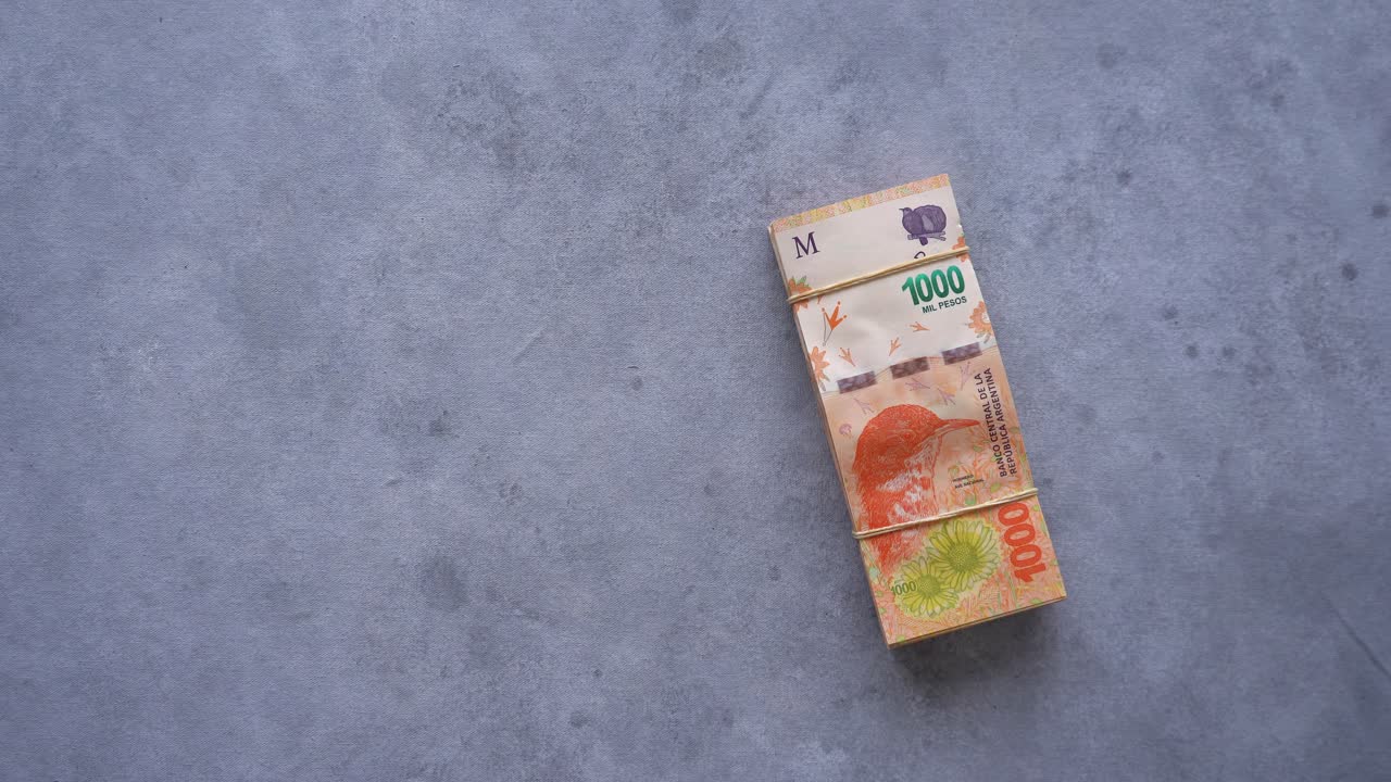 Ruka pokládající stoh argentinských bankovek v hodnotě 1000 pesos na stůl.