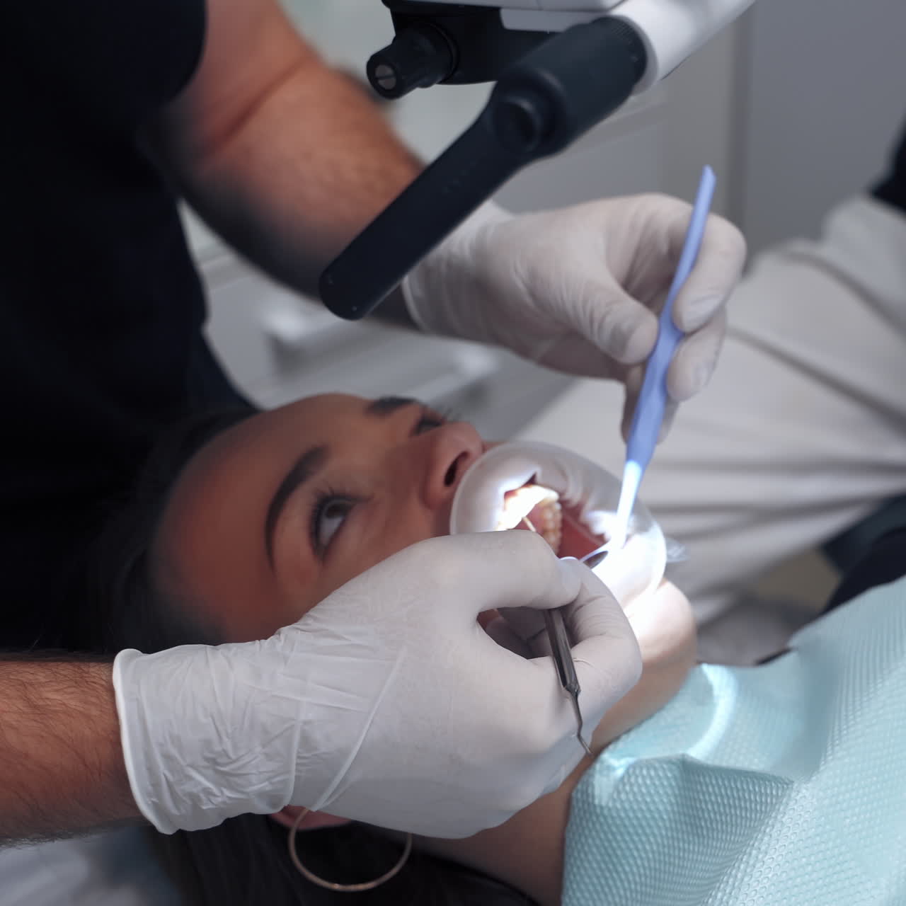 Dentist with assistant treating female's teeth. Medical tools in doctors hands during patient's teeth check up. Woman visits stomatologist. Close-up.