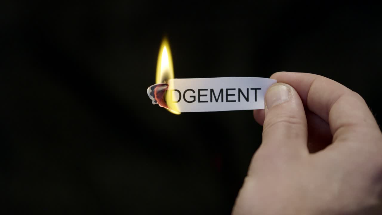 Burning Away Judgment - Hand Setting Fire to Paper note Marked “JUDGEMENT”, Powerful Release of Criticism, Guilt and Shame, Dark Cinematic Close-Up. Mental health, therapy