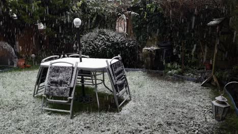 heavy wintertime snow falling on disused garden table and chairs in cold suburban residence