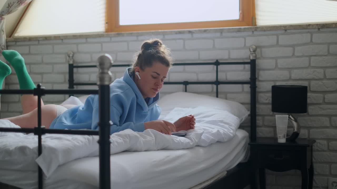 Woman relaxing in bed with earbuds and phone