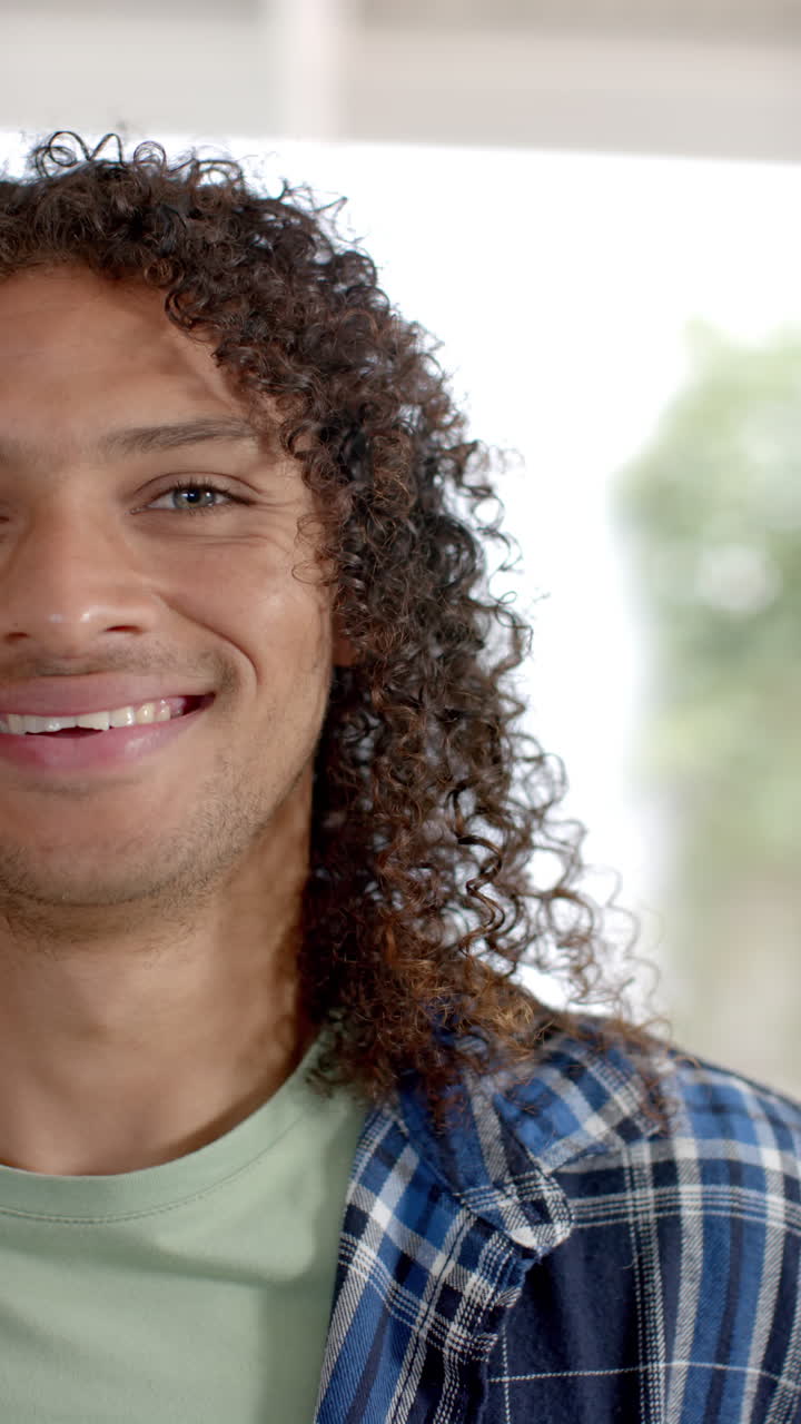 Vertical video of portrait of biracial man with long curly hair at home, slow motion