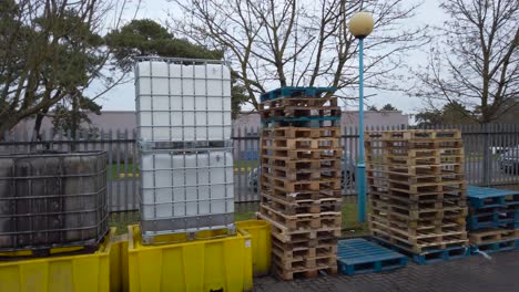 Empty-IBC-chemical-containers-and-pallets-stacked-outside-of-a-factory---panning-shot