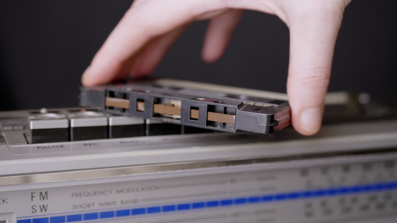 남성의 손은 오래된 오디오 카세트를 빈티지 테이프 레코더의 버튼에 넣습니다.
