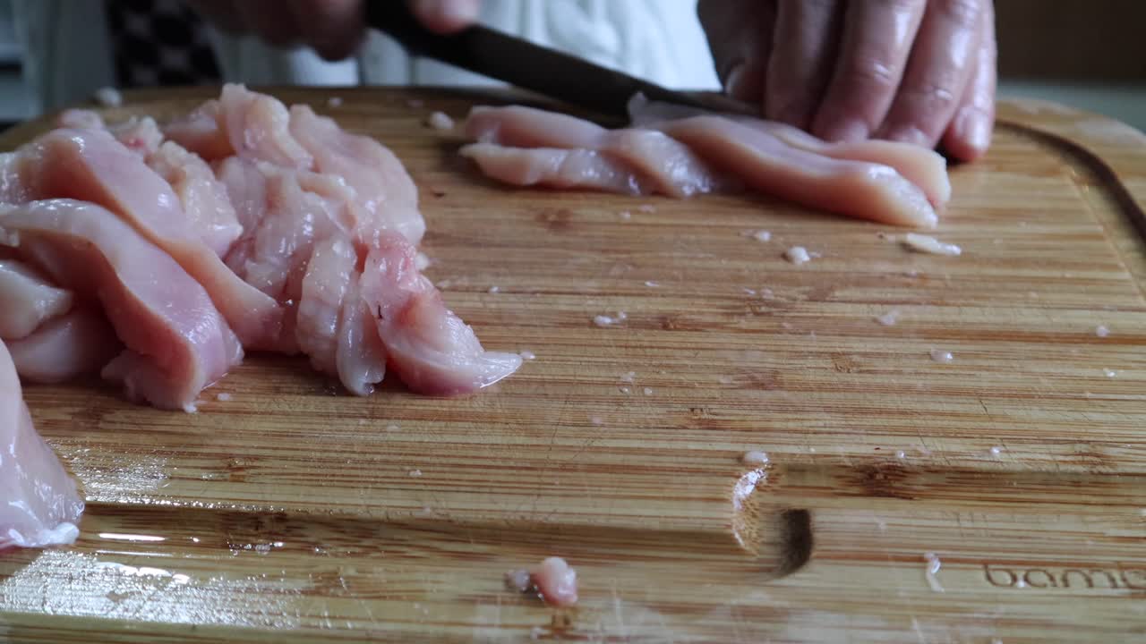 Tagliare carne di pollo fresca verticalmente su un tagliere di legno in cucina