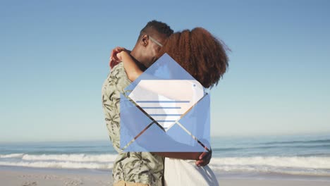 Animation-of-email-envelope-digital-icon-over-couple-in-love-hugging-on-beach