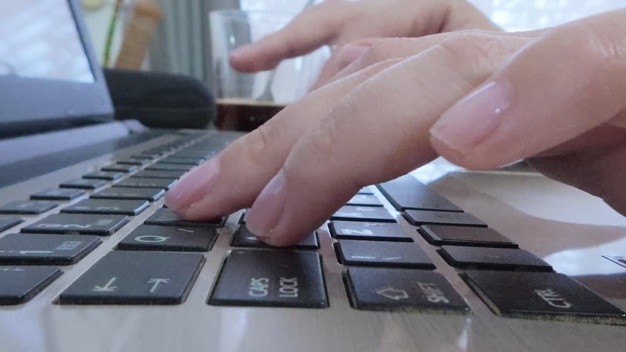 Female hands actively using a laptop, typing on the keyboard from a side view