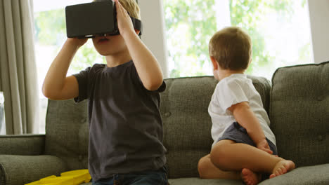 boy sitting on sofa while brother using virtual reality headset 4k