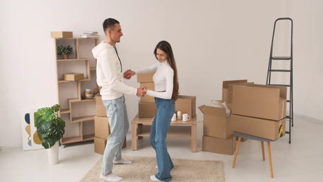 front view of a young happy couple barefoot dancing together on carpet in a new house