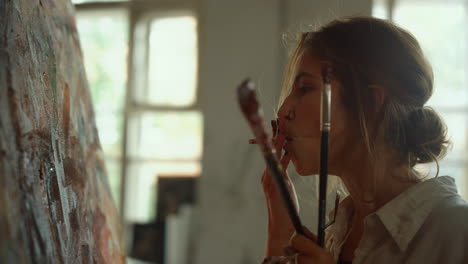 tired woman smoking cigarette indoors. serious painter holding paintbrushes.