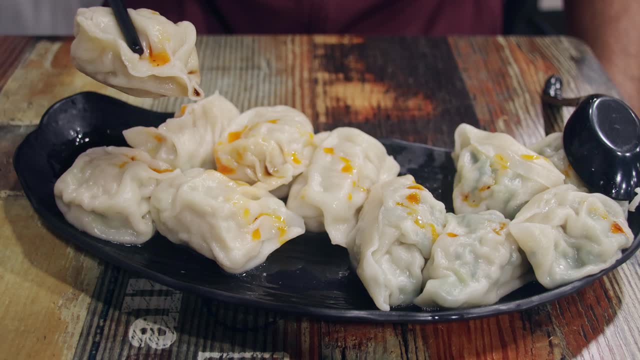 Sepiring momo atau pangsit tradisional Nepal dengan saus cabai di atas meja kayu, diambil dengan sumpit. Pengalaman nyata menyantap makanan lokal autentik dari Nepal