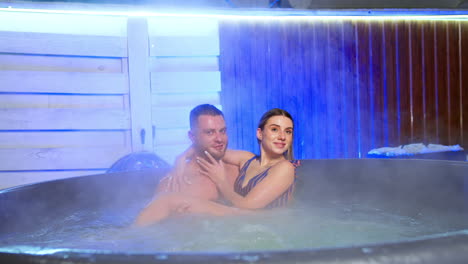 bearded caucasian man holds a beautiful long-haired woman in hands sitting in hot tub. happy couple in love in spa.