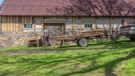 Worker-nails-wood-slats-onto-cinder-block-farm-wall-as-tree-and-cloud-shadows-pass-over