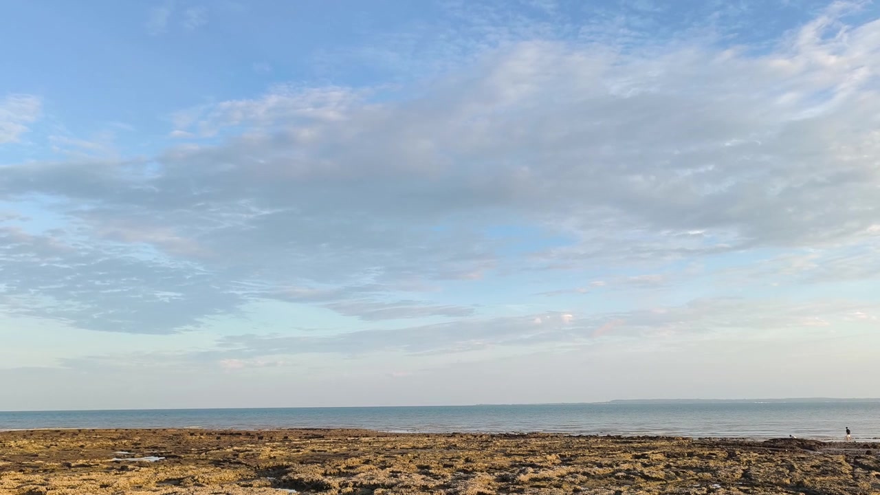 Vista serena sull'oceano con costa rocciosa e cielo azzurro nuvoloso