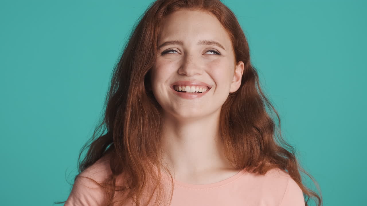una chica pelirroja frente a la cámara sobre un fondo turquesa.