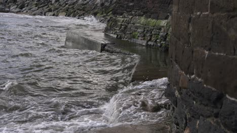 las olas chocan contra la pared rocosa de piedra en cámara lenta causando choques y salpicaduras en un día gris nublado dando una sensación de miedo de mal humor