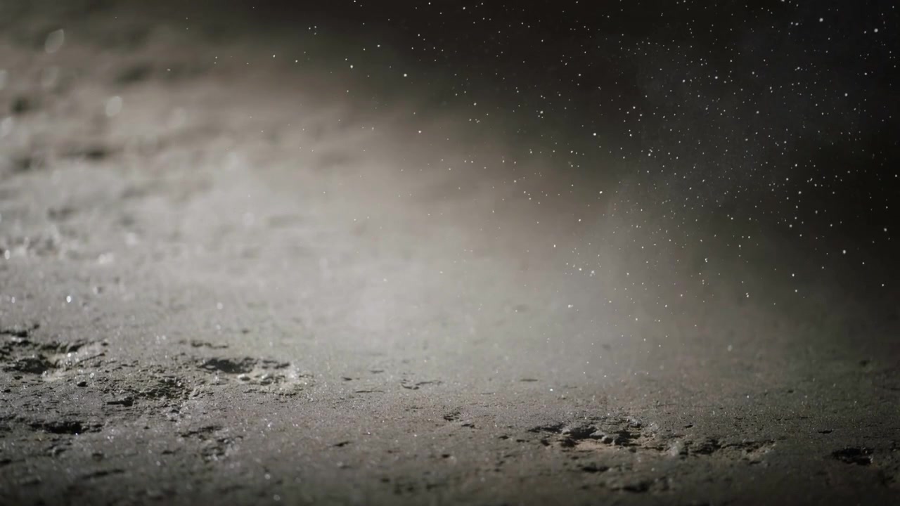 Un disturbo transitorio che solleva un velo sulla terra polverosa e texturizzata a bassa angolazione, creando un effetto bokeh.