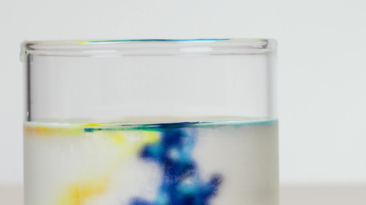 Macro view of colored liquid diffusing in a glass beaker against a white background