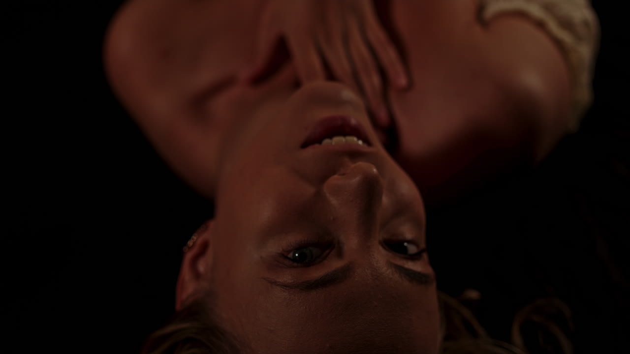 A beautiful woman lies in a dark room, she opens her eyes and sensually looks at the camera while stroking her attractive body