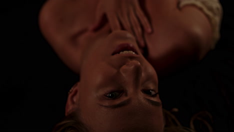 a beautiful woman lies in a dark room, she opens her eyes and sensually looks at the camera while stroking her attractive body
