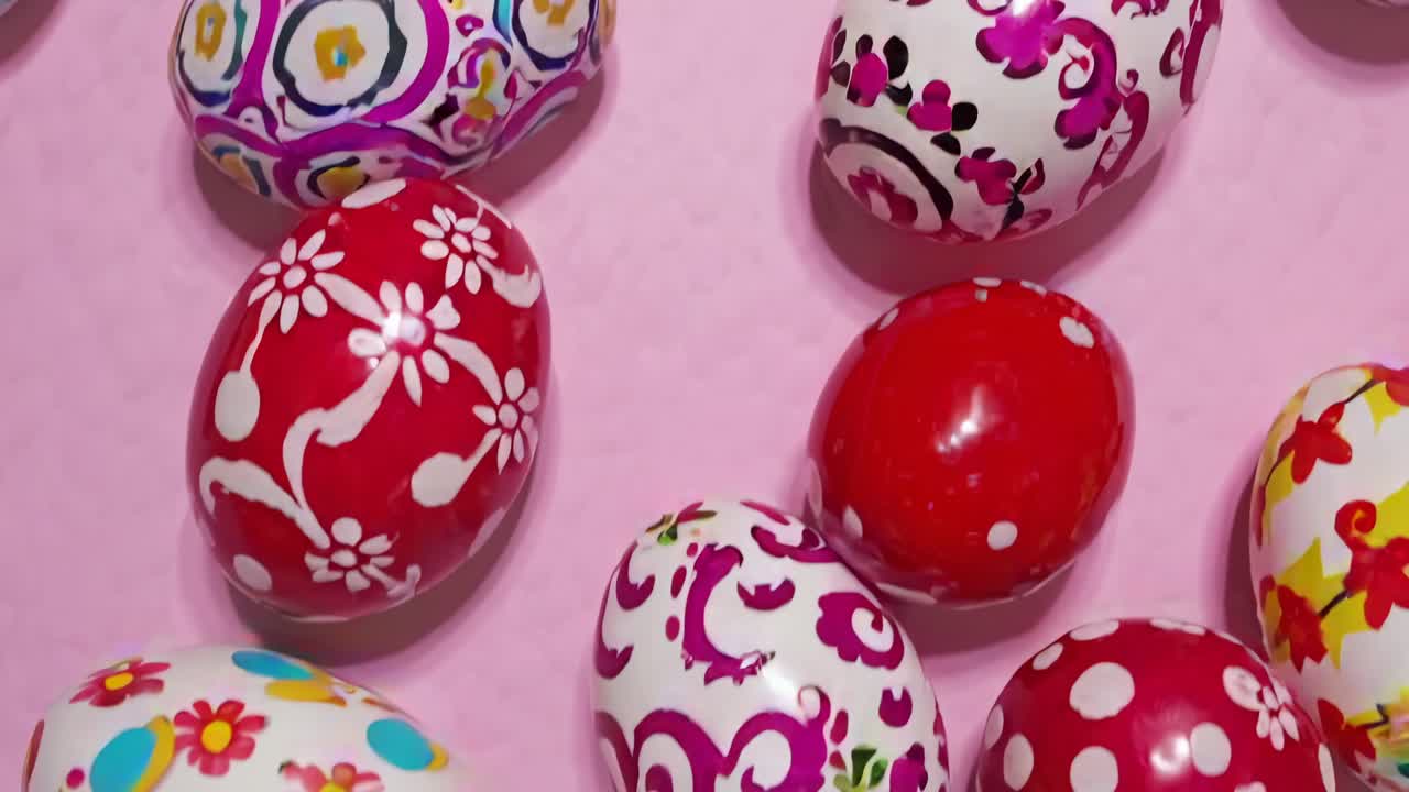 Colorful, patterned Easter eggs scattered on a pink background, captured from a top-down angle