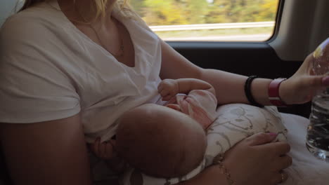 mother breastfeeding baby and drinking water in the car