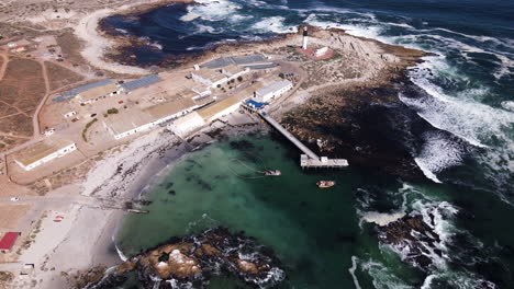 El-Arco-Aéreo-Muestra-La-Ensenada-De-La-Freidora,-El-Faro,-El-Pueblo-Pesquero-De-Doringbaai