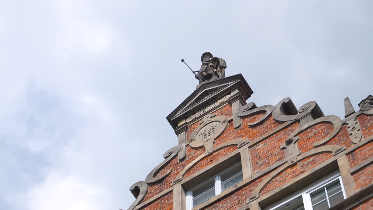 Stone statue of a historic figure on top of ornate red brick building in Gdansk