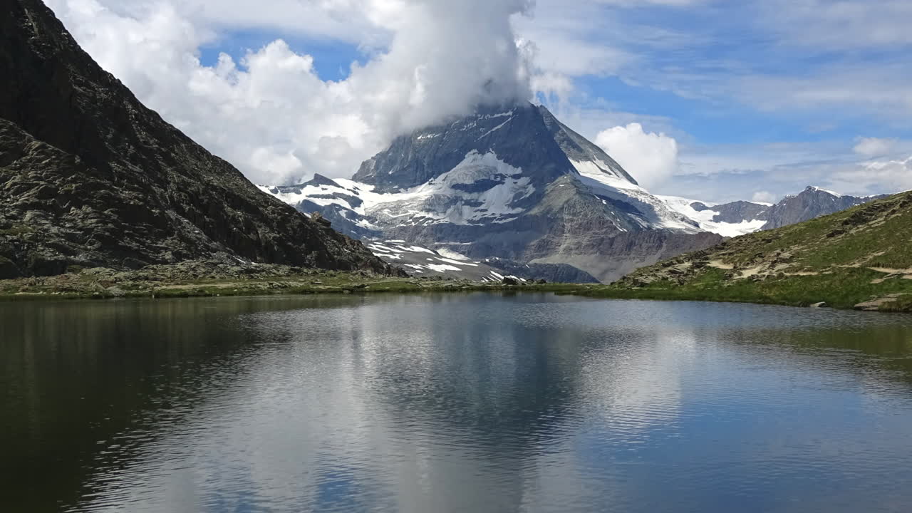 Ripresa in timelapse di nuvole che fluttuano intorno al Cervino sopra un tranquillo lago alpino a Zermatt, Vallese, Svizzera, che riflette le montagne e il mutevole clima estivo