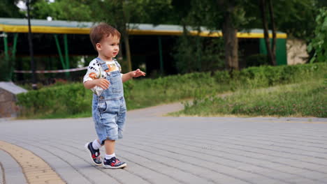 little kid stands outside watching the pigeon walk by the paved road. happy baby runs in summer park.