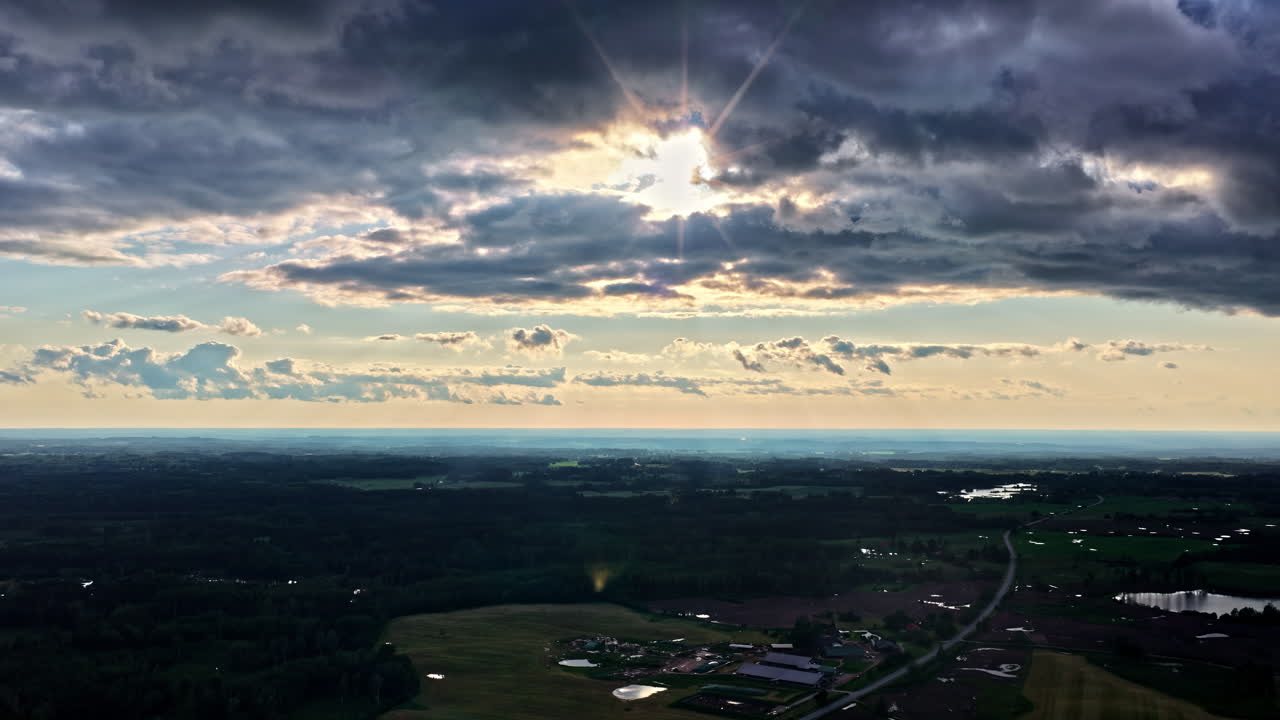 Dark stormy clouds with sun rays shining through above Latvia landscape, aerial view