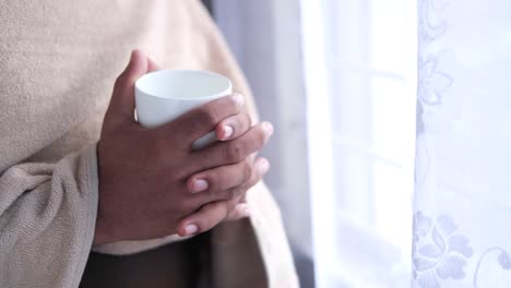 person holding a warm drink by the window