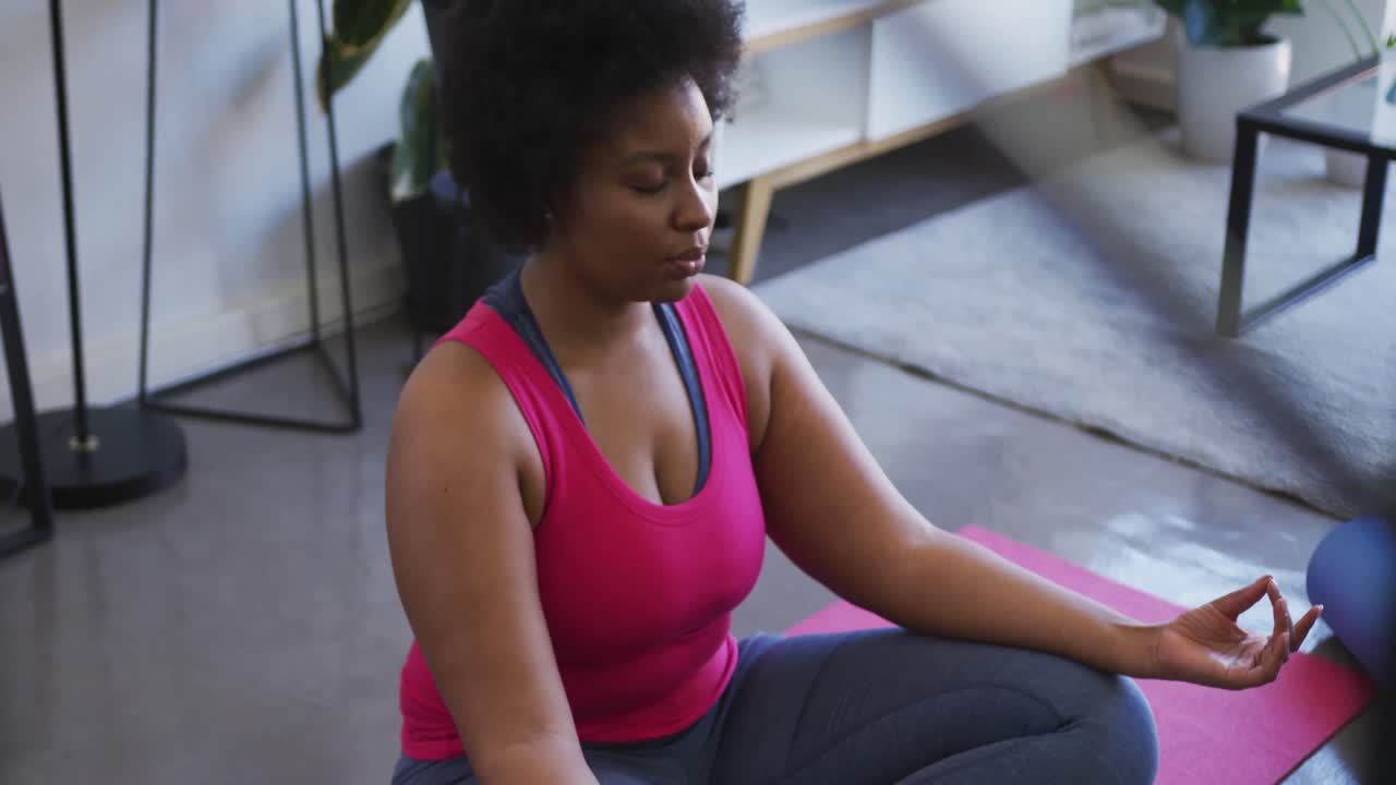 mujer afroamericana de tamaño grande sentada en una alfombra de ejercicio meditando