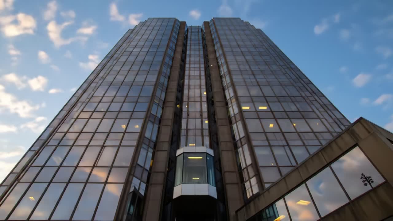 A Modern Glass Office Tower Gleaming Under a Cloudy Sky, Showcasing Urban Architecture and Reflective Surfaces in Dynamic Lighting Conditions