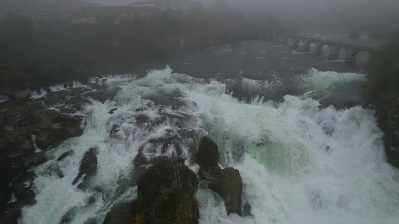 Misty aerial panorama capturing Rhine Falls cascading near Laufen Castle, revealing dramatic Swiss landscape shrouded in morning fog